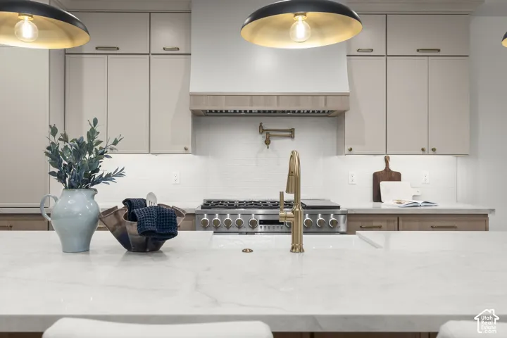 Kitchen featuring a large island with a light-toned countertop, a professional-grade range, a pot filler, a wood-trimmed range hood, and pendant lighting