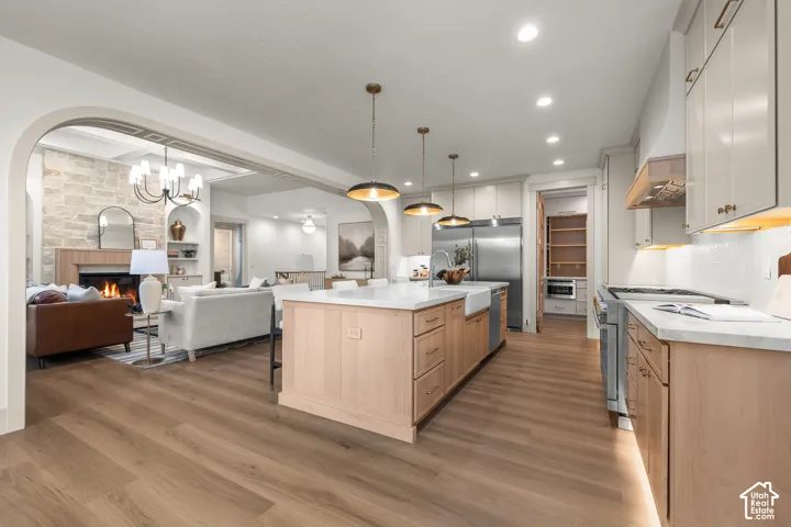 Open-concept kitchen and living area featuring a large center island with wood cabinetry, stainless steel appliances, pendant lighting, and wood-finish flooring throughout