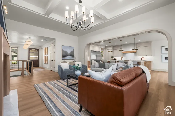 Coffered ceiling with a chandelier, wood-finish flooring, staircase with dark wood newel posts, arched entryway, and recessed lighting