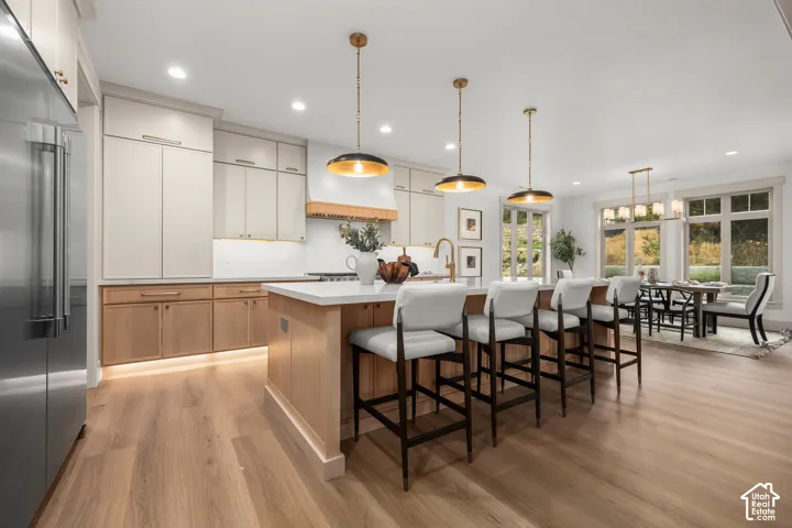 Expansive kitchen island with seating for four, light wood-finish flooring, recessed lighting, and stainless steel appliances