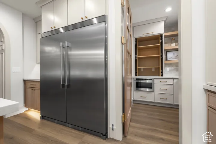 Stainless steel refrigerator, wood-finish flooring, light cabinetry, built-in microwave, and arched doorway