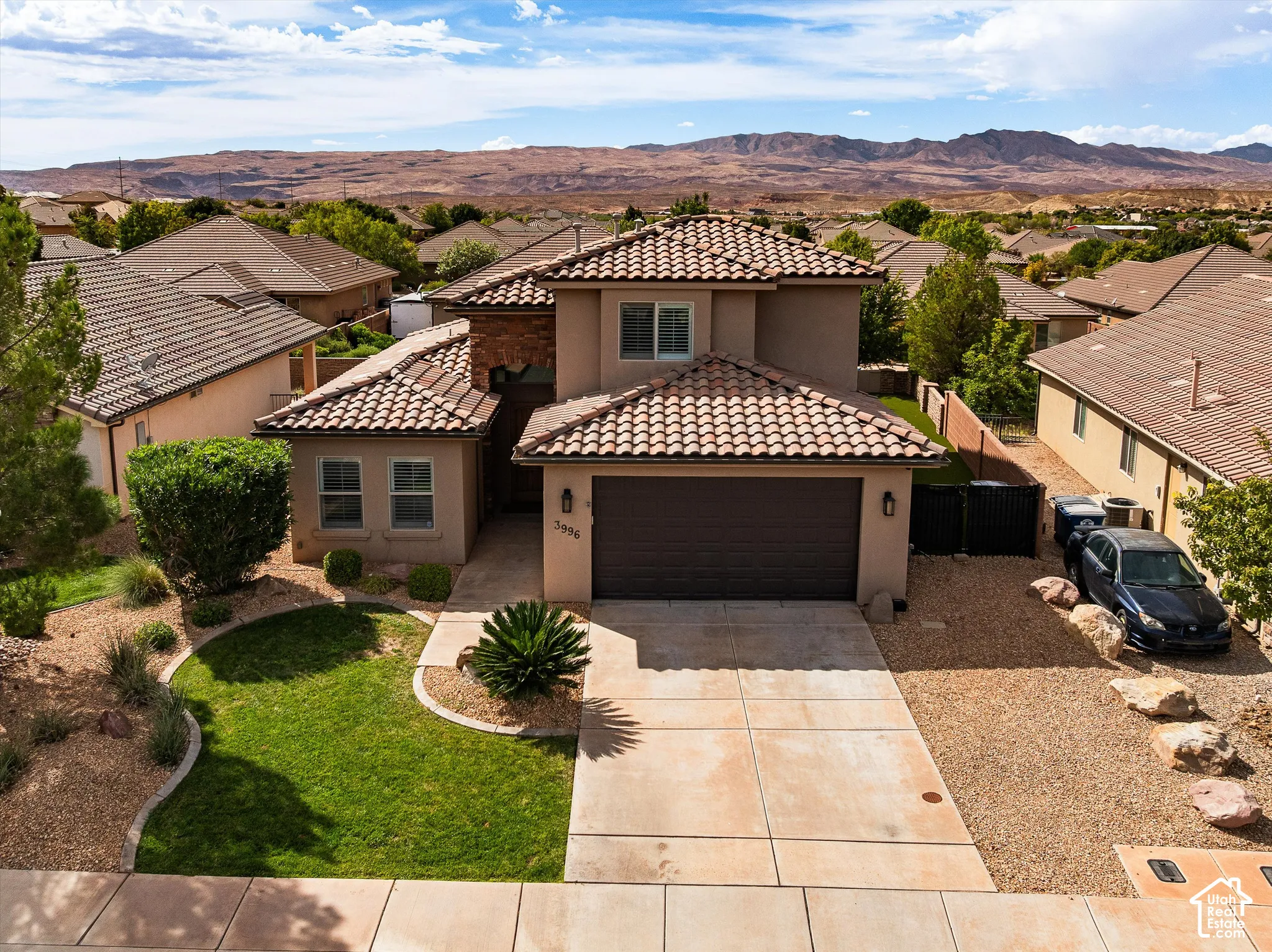 Mediterranean-style architecture with a tile roof, stucco exterior, and attached garage, tile roofing, private swimming pool, artificial turf, and mature landscaping