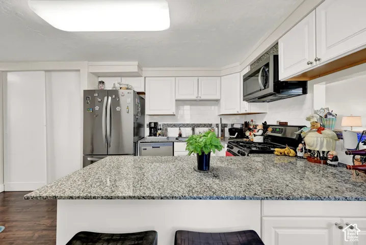 Kitchen featuring white cabinetry, granite countertops, stainless steel refrigerator, stainless steel microwave, and wood-finish flooring