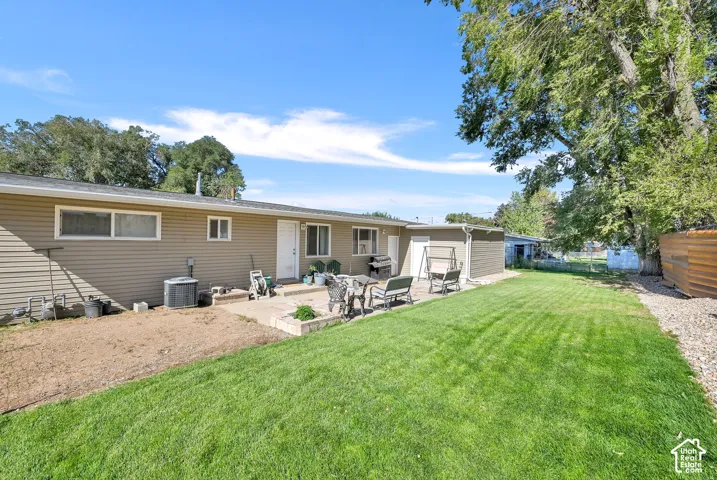 Expansive rear yard featuring a large concrete patio, manicured lawn, and mature trees