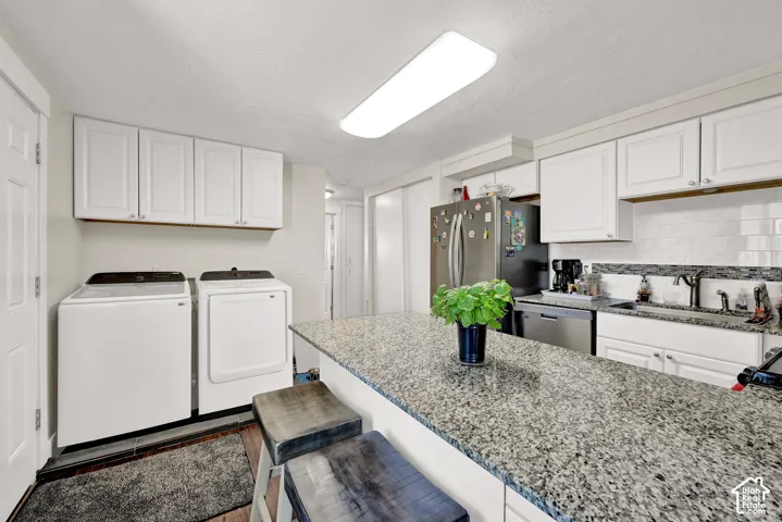 Kitchen with a granite-finish island, white cabinetry, integrated stainless steel appliances, and a subway tile backsplash