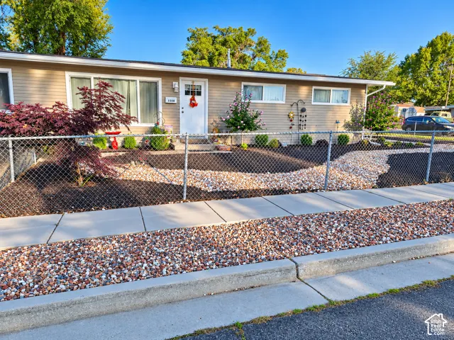 Low-maintenance front exterior featuring a single-story ranch-style home with neutral siding, metal fencing, and drought-resistant rock landscaping