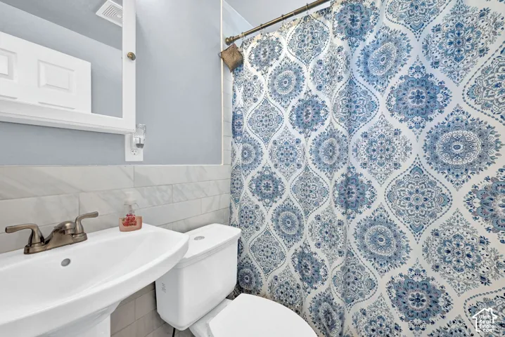 Pedestal sink with a two-handle faucet, white toilet, and light-toned wall tile