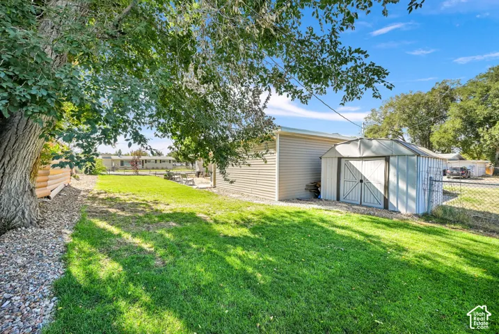 Expansive backyard featuring a manicured lawn, established shade tree, gravel landscaping, and a utility shed
