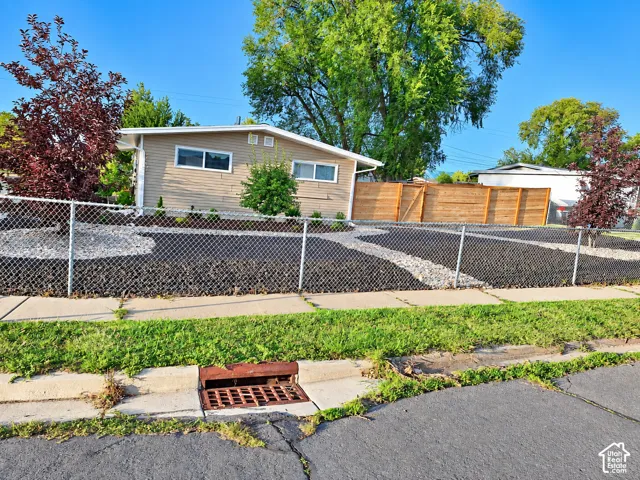 Charming mid-century home with updated siding and modern windows, situated on a landscaped lot featuring mature trees, established plantings, and a chain-link perimeter fence