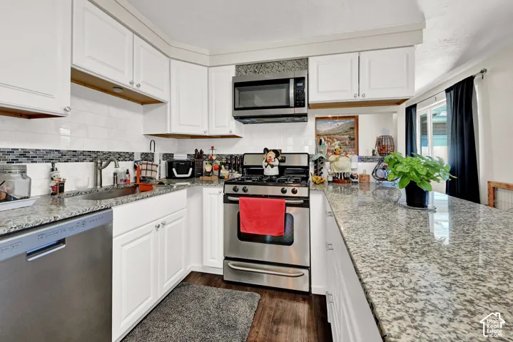 White cabinetry with stainless steel appliances, granite countertops, and a tile backsplash