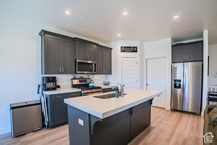 Kitchen featuring dark gray cabinetry, stainless steel appliances, a center island with sink, light wood-finish flooring, and recessed lighting
