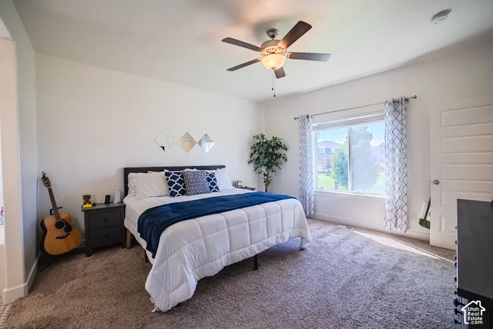 Light-filled bedroom with a ceiling fan, a large window, and light-colored carpeting