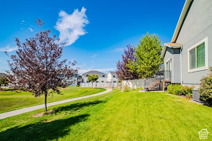 Expansive manicured lawn with mature trees, paved walking path, and a private deck with stairs