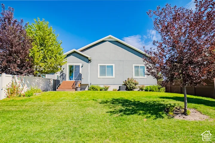 Expansive green lawn with mature trees, privacy fencing, and a rear exterior featuring a sliding glass door and multiple windows