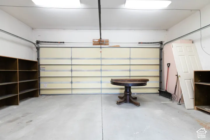 Concrete flooring with a segmented garage door, overhead lighting, and built-in shelving