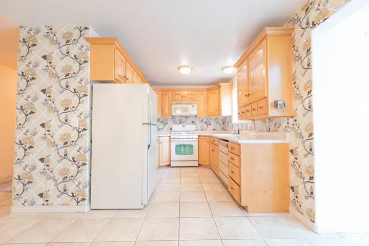 U-shaped kitchen layout featuring light wood-finish cabinetry, tile flooring, and a patterned wallpaper accent