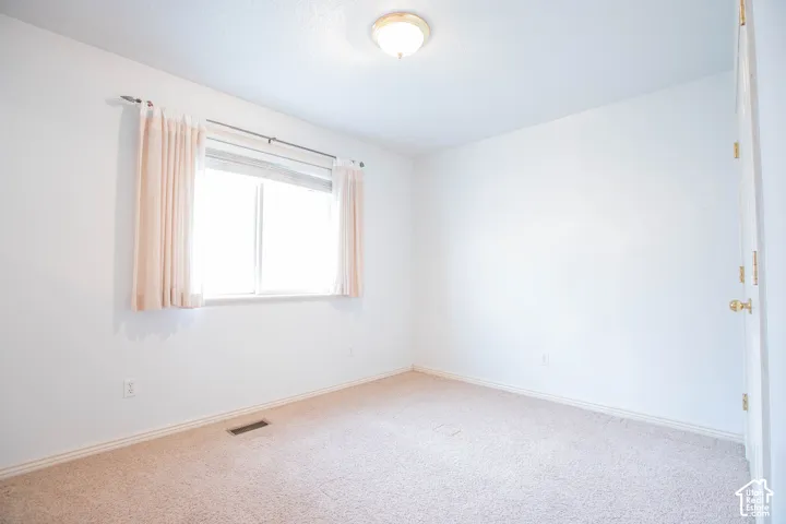 Neutral-toned carpet flooring, white painted walls, and a single window with curtain rods