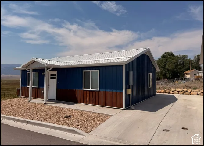 Exterior featuring a metal roof, blue and wood-finish siding, a covered entry, and a concrete driveway