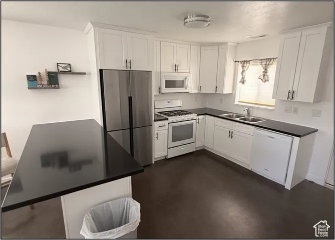 White shaker cabinetry with dark hardware, stainless steel refrigerator, dark countertops, built-in microwave, and a gas range