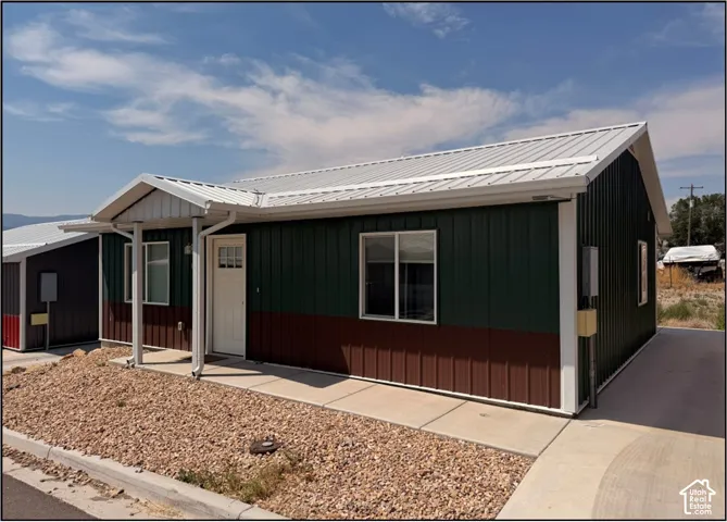 Two-tone corrugated metal siding with white trim, a covered entry, concrete walkway, and gravel landscaping