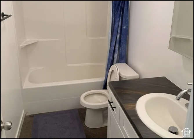 Full bathroom featuring a ceramic pedestal sink with chrome faucet, an alcove bathtub with shower surround and blue shower curtain, wood-finish vanity cabinetry, and dark tile flooring