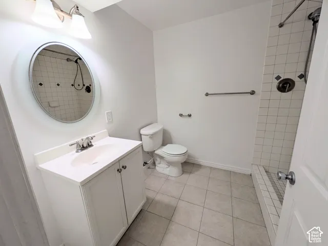 White vanity with integrated sink, coordinating wall mirror, overhead vanity lighting, and tiled shower surround