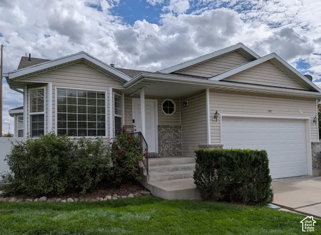 Beige siding exterior with stone accents, bay window with louvered blinds, attached two-car garage, concrete porch steps, and front yard landscaping