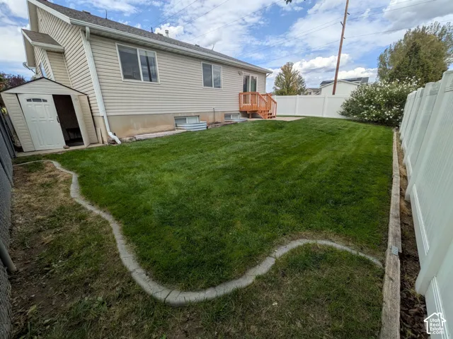 Expansive backyard featuring a manicured lawn, white privacy fencing, and a permanent storage shed