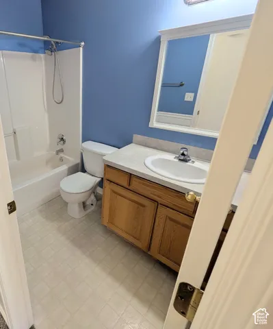 White tub/shower combination, single vanity with wood-finish cabinetry, integrated sink, and a framed mirror with overhead lighting