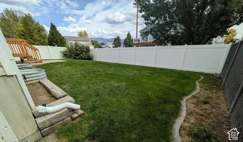 Expansive backyard featuring a manicured lawn, white privacy fencing, and wood-finish deck stairs