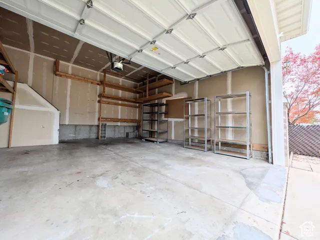 Concrete flooring with a white paneled garage door and integrated shelving