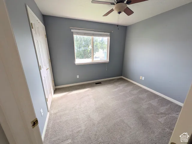 Gray carpeting with white baseboards, a window with window treatments, a ceiling fan with integrated lighting, and bi-fold closet doors