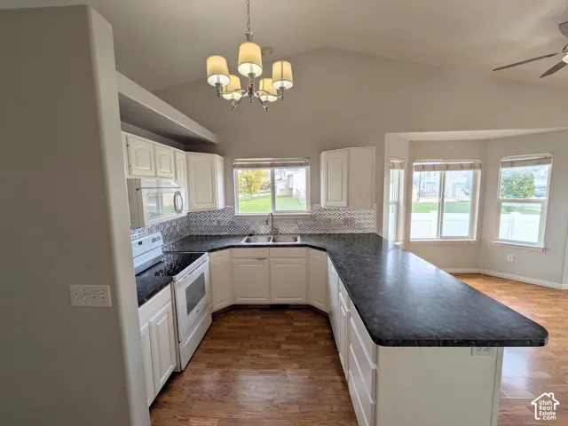 Vaulted ceilings, white cabinetry, dark countertops, patterned backsplash, and wood-finish flooring