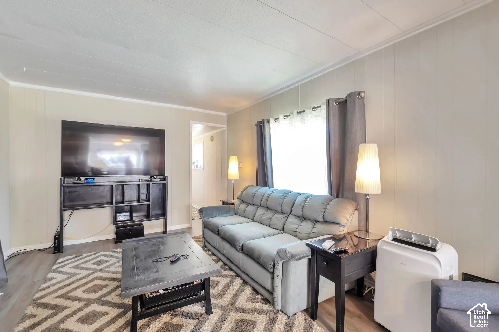Paneled walls with crown molding, wood-finish flooring, and a large window with privacy coverings