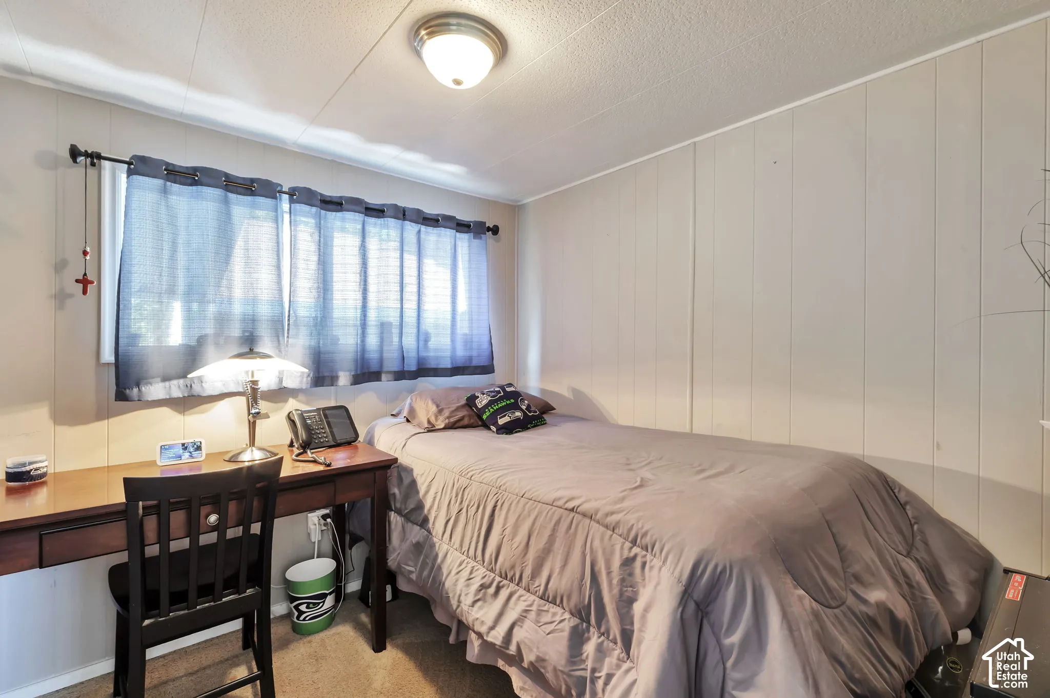 Textured ceiling, wall paneling, window with curtain rod, ceiling-mounted light fixture, and carpet flooring