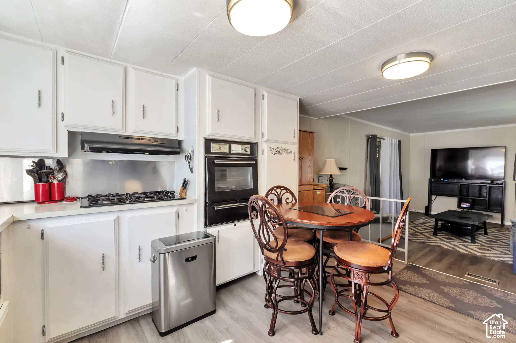 White cabinetry, integrated wall oven, gas cooktop, wood-finish flooring, and recessed lighting