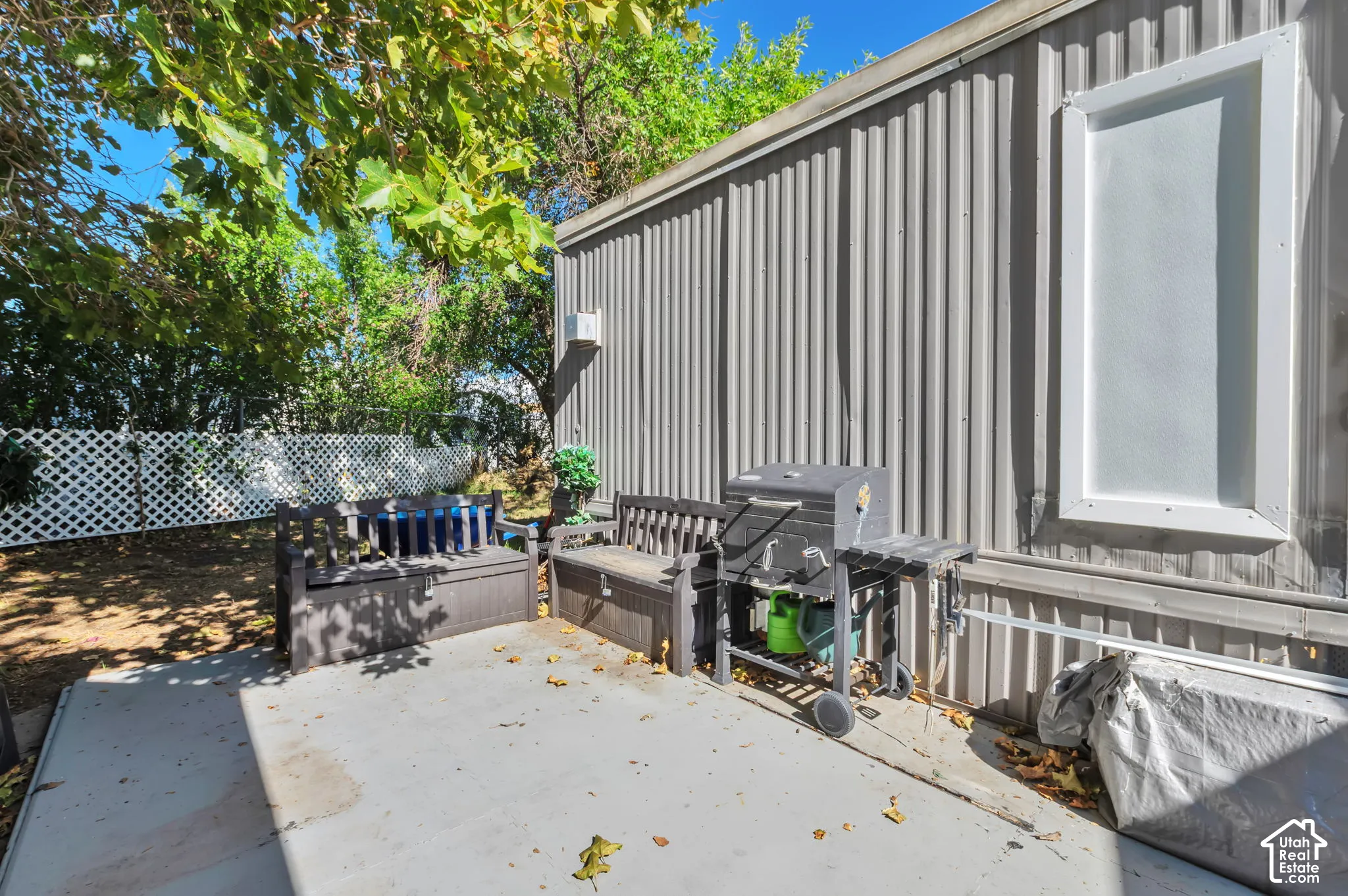 Concrete patio area with a privacy fence, mature trees, and vertical panel siding