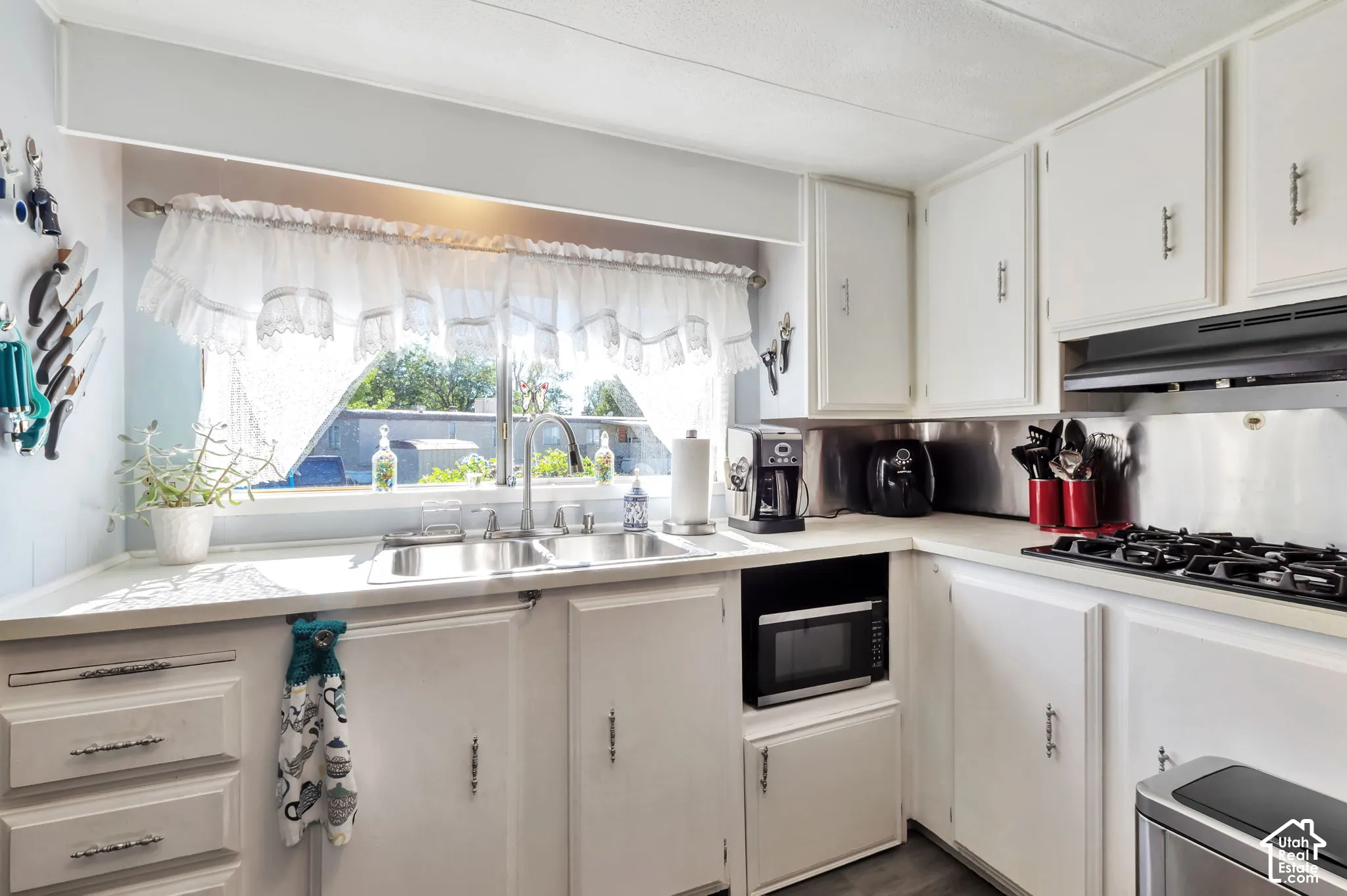 White cabinetry with silver hardware, dual basin stainless steel sink, built-in microwave, and a four-burner cooktop with ventilation hood