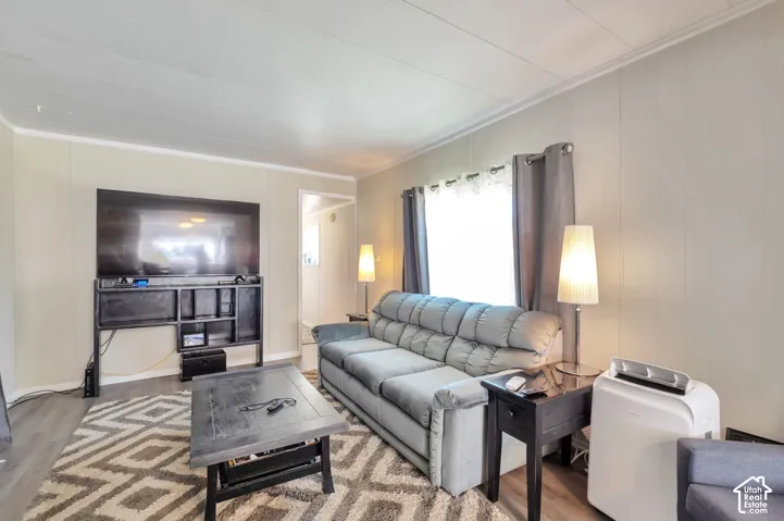 Paneled walls with crown molding, wood-finish flooring, and a large window with privacy coverings