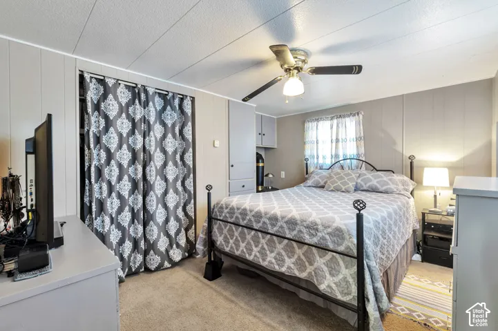 Carpeted bedroom with a ceiling fan, built-in cabinetry, and vertical wall paneling
