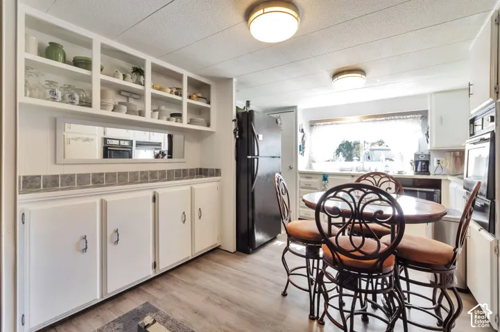 Kitchen with wood-finish flooring, built-in white cabinetry, open shelving, and a dual basin sink beneath a window