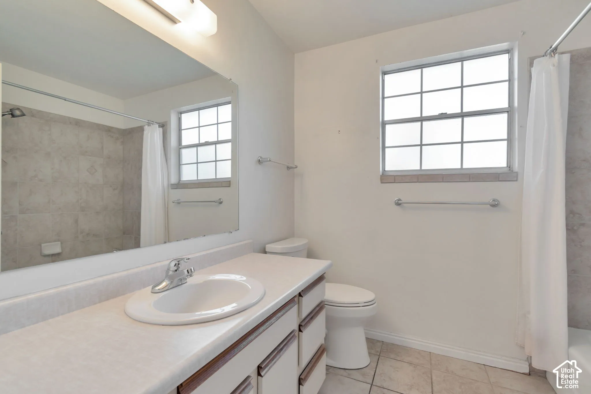 Vanity with integrated sink, tile flooring, window with grid pattern, overhead lighting, and tiled shower surround