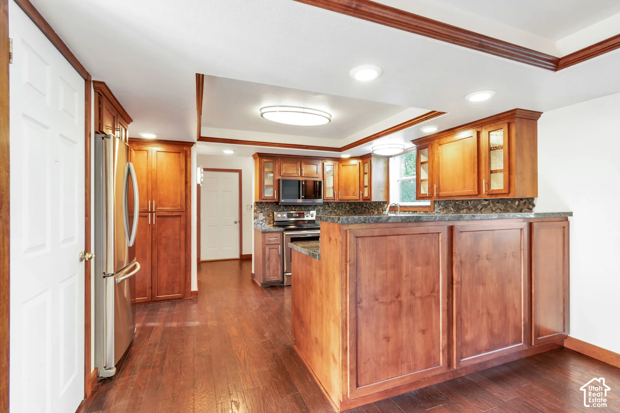 Spacious kitchen featuring wood-finish flooring, abundant wood cabinetry, integrated stainless steel appliances, and solid surface countertops