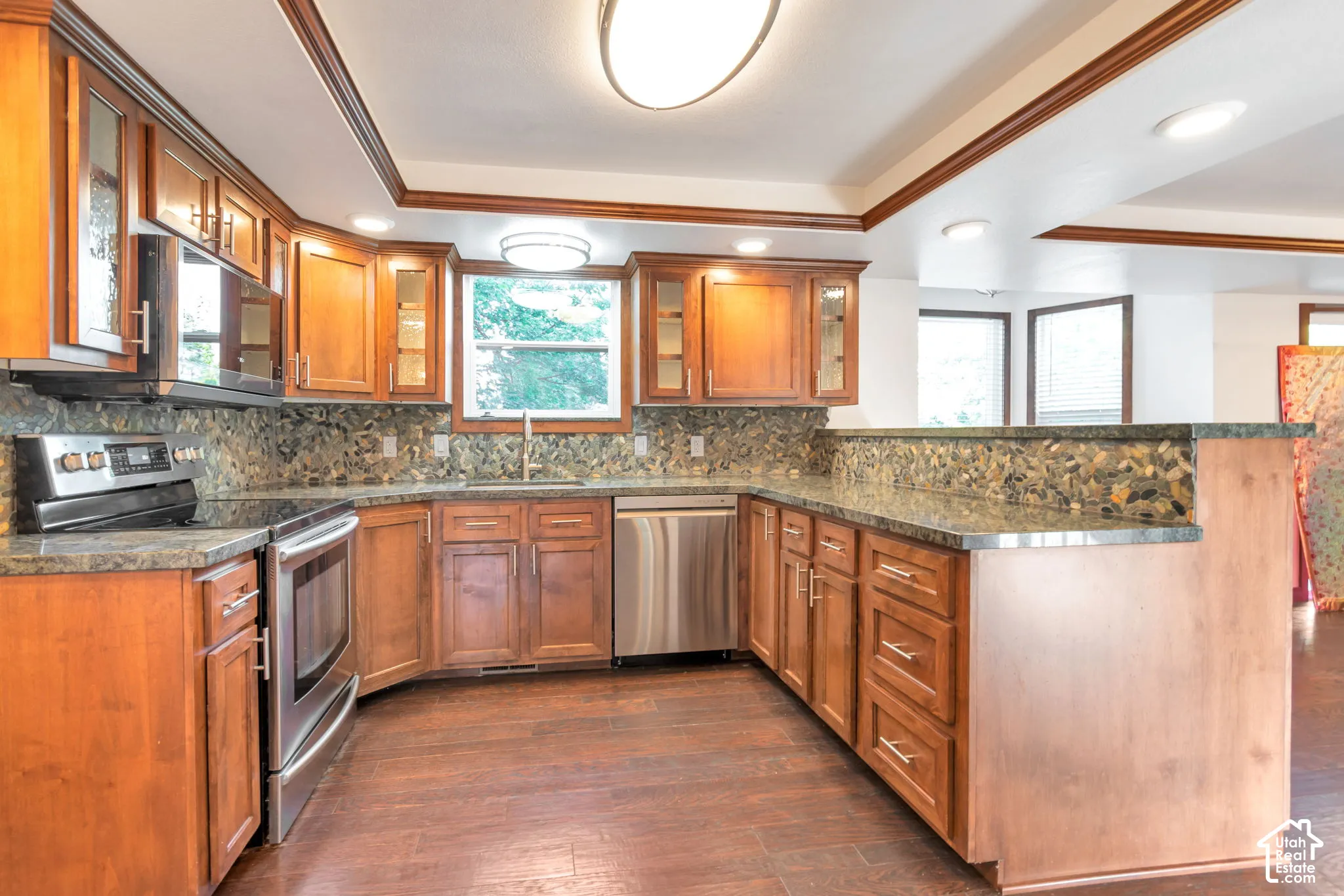 Kitchen featuring wood cabinetry, stainless steel appliances, stone countertops, and a full-height backsplash