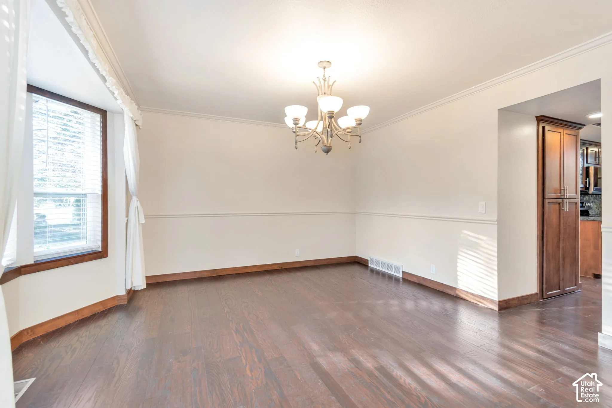 Wood-finish flooring, bay window, chandelier lighting, crown molding, and wainscoting