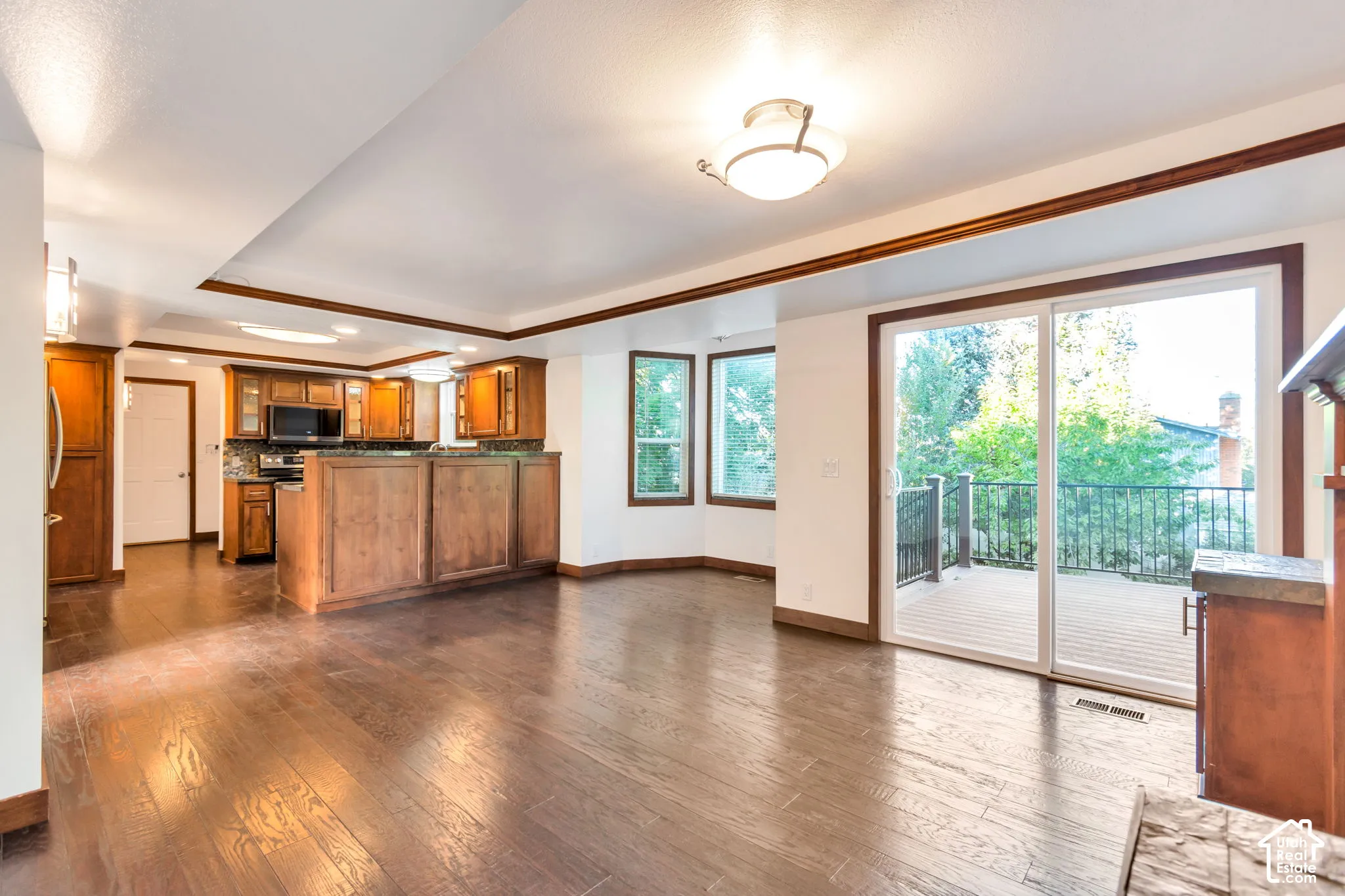 Wood-finish flooring, recessed ceiling with trim, kitchen with wood cabinetry and dark countertops, bay windows, and sliding glass door access to an outdoor deck