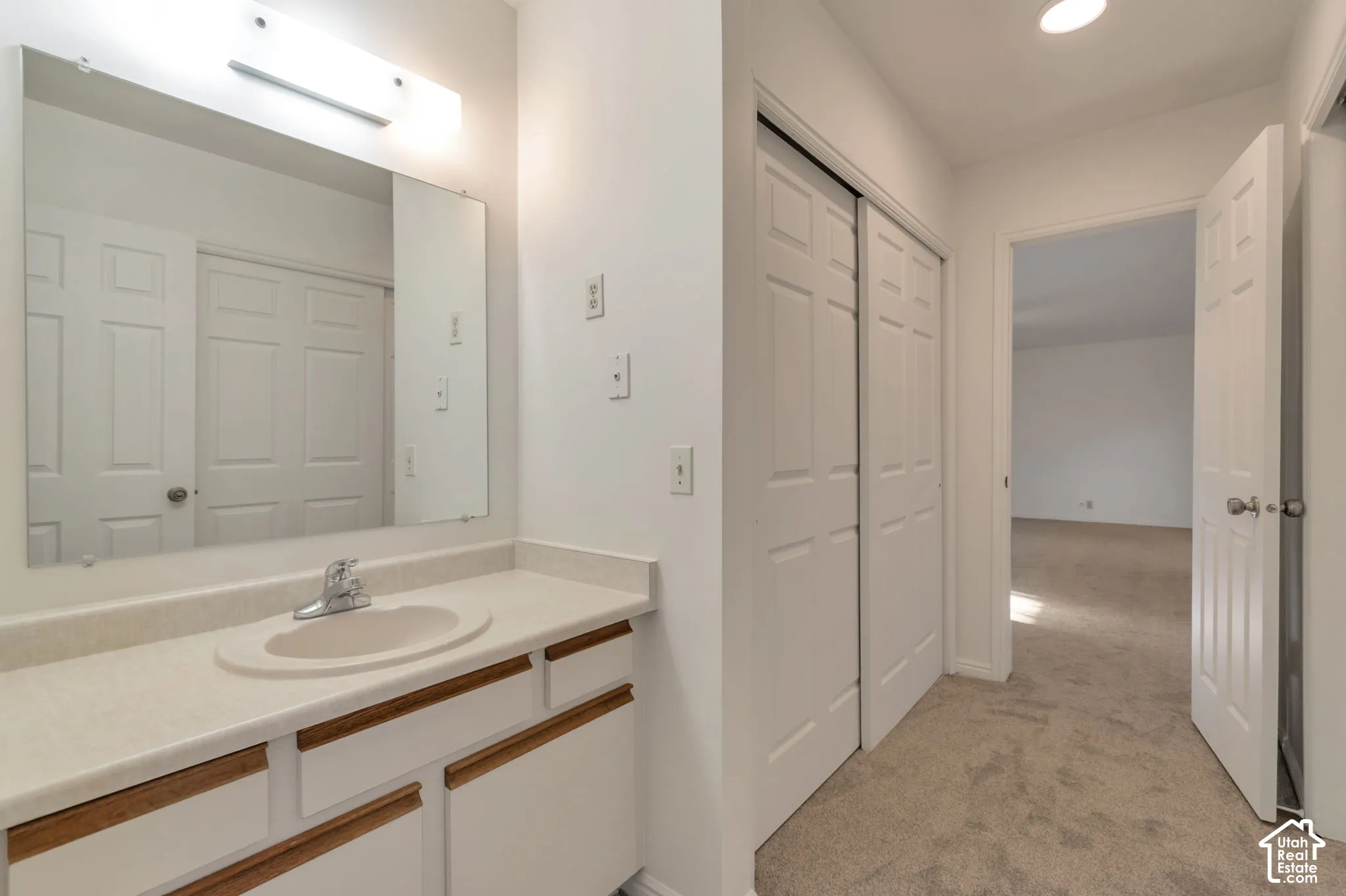 Vanity with integrated sink, wall-mounted mirror, overhead light fixture, and white cabinetry
