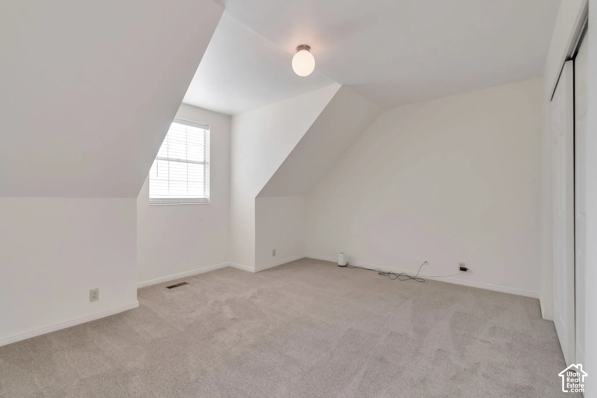 Carpeted room featuring a window with blinds, sloped ceilings, and a flush-mount ceiling light