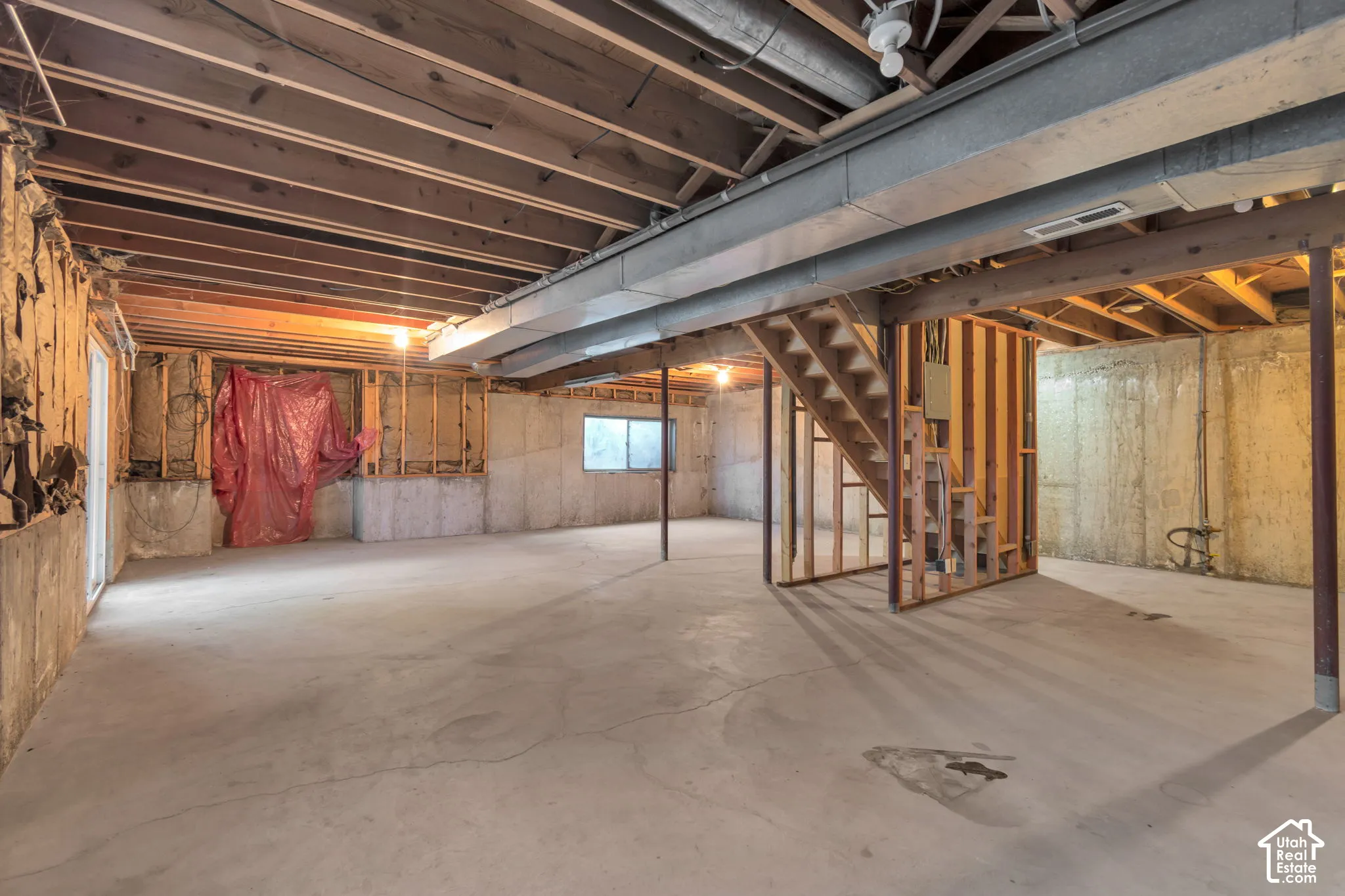 Expansive unfinished basement featuring concrete flooring, exposed ceiling joists, and a partial wood-framed staircase