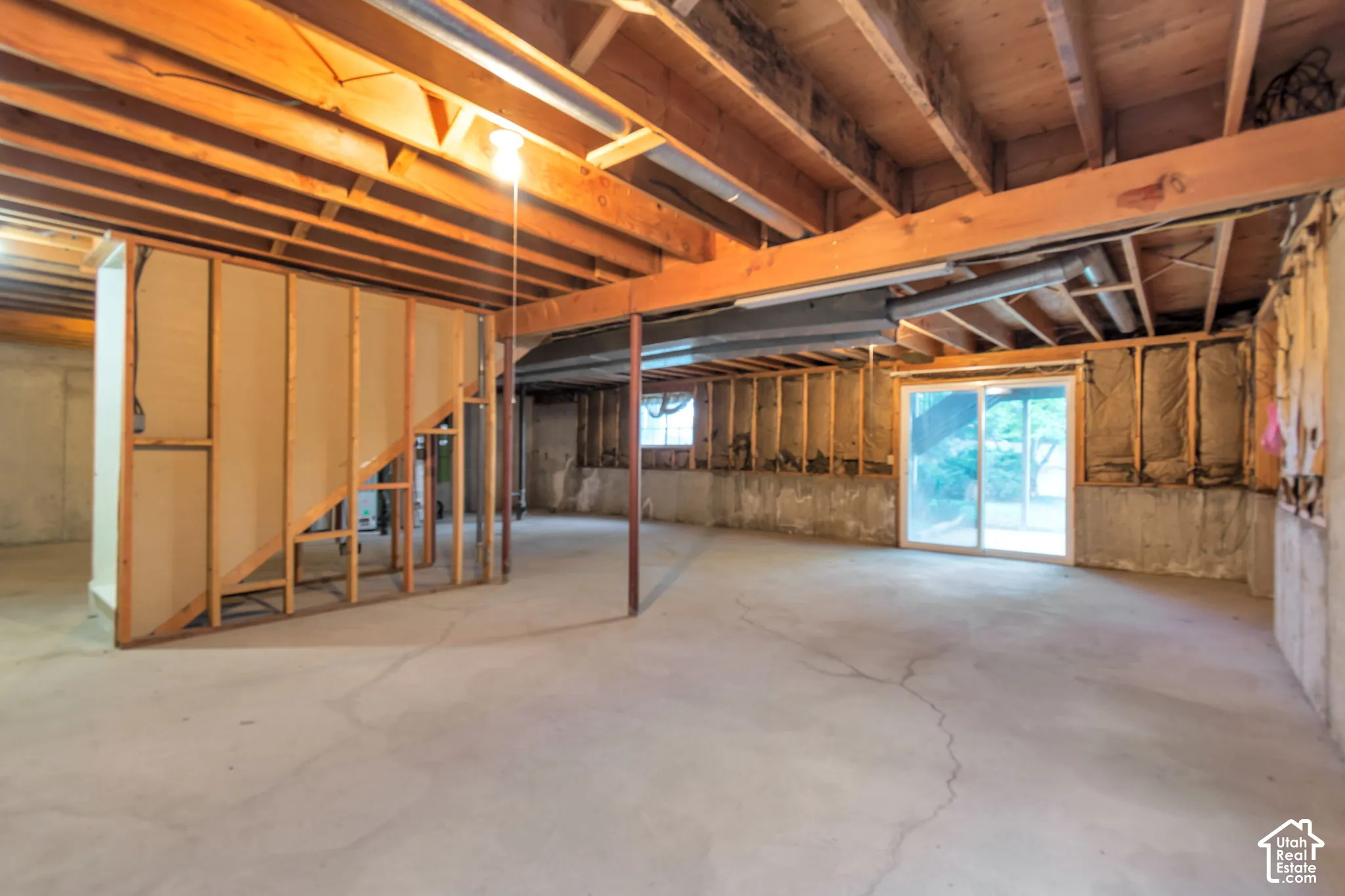 Unfinished basement with exposed ceiling joists and support beams, concrete flooring, framed interior walls, and a sliding glass door